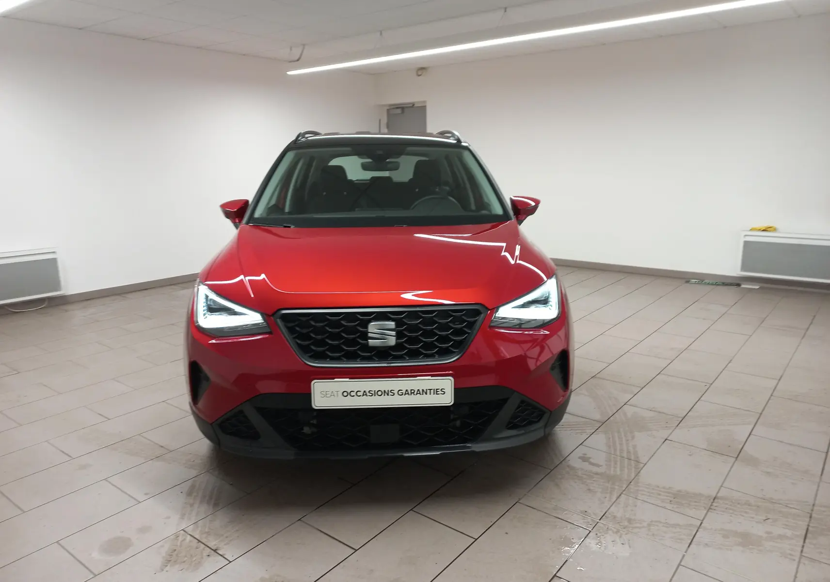 Vue frontale d'un SEAT Arona 2025 rouge Désir avec toit noir Minuit, feux LED allumés en intérieur.