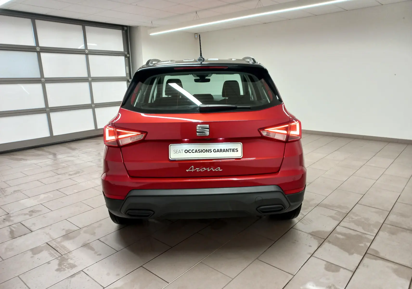 Vue arrière d'un SEAT Arona rouge Désir avec toit noir Minuit, dans un garage lumineux au sol carrelé.