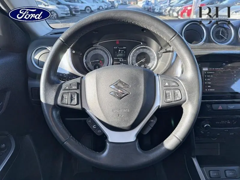 Vue intérieure centrée sur le volant cuir multifonction noir du Suzuki Vitara 1.4 Boosterjet Hybrid, tableau de bord et écran tactile visibles.