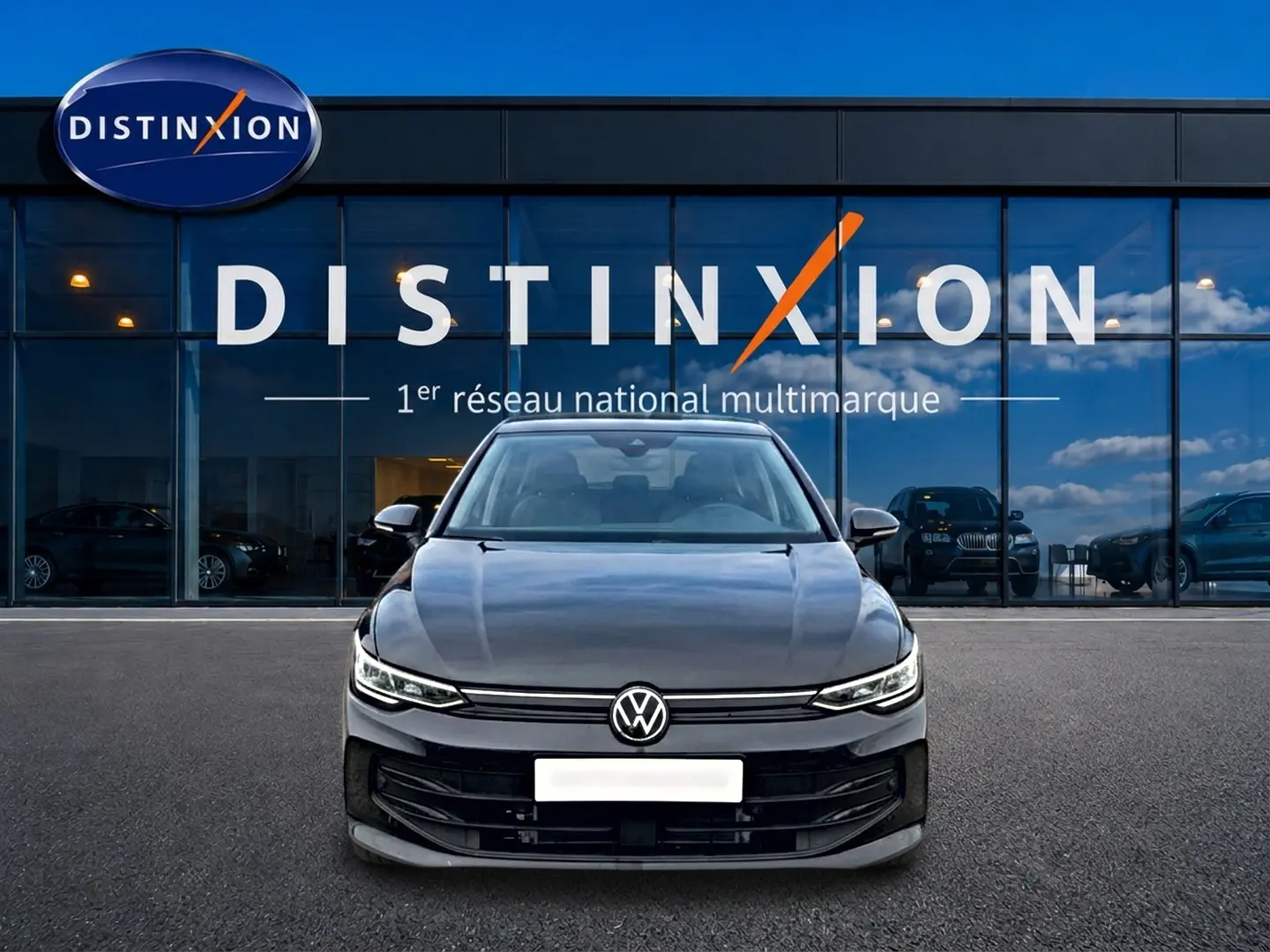 Vue frontale d'une Volkswagen Golf noire 2026 garée devant une vitrine avec logo Distinxion en arrière-plan.