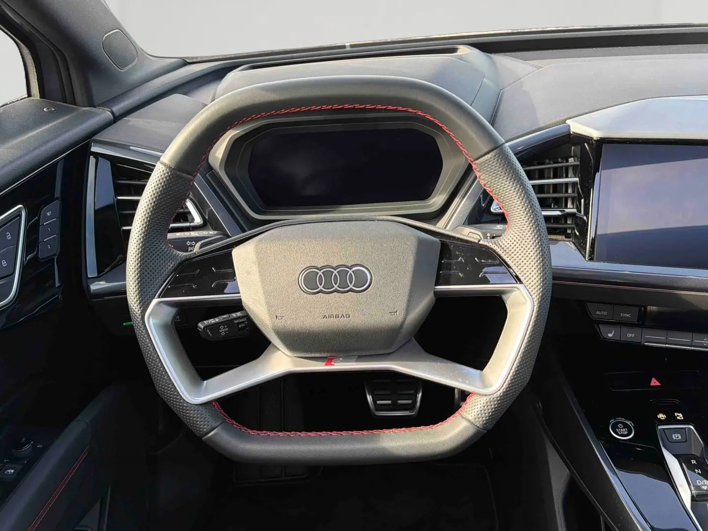 Volant multifonction noir avec surpiqûres rouges dans l'habitacle d'un Audi Q4 e-tron 2025, tableau de bord et écran tactile visibles.