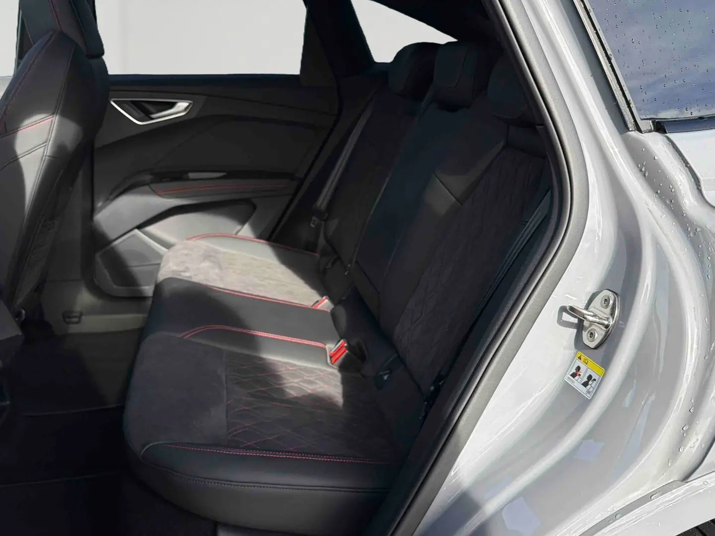 Vue intérieure côté arrière droit de l'Audi Q4 e-tron gris galet, montrant les sièges arrière en tissu noir avec surpiqûres rouges.