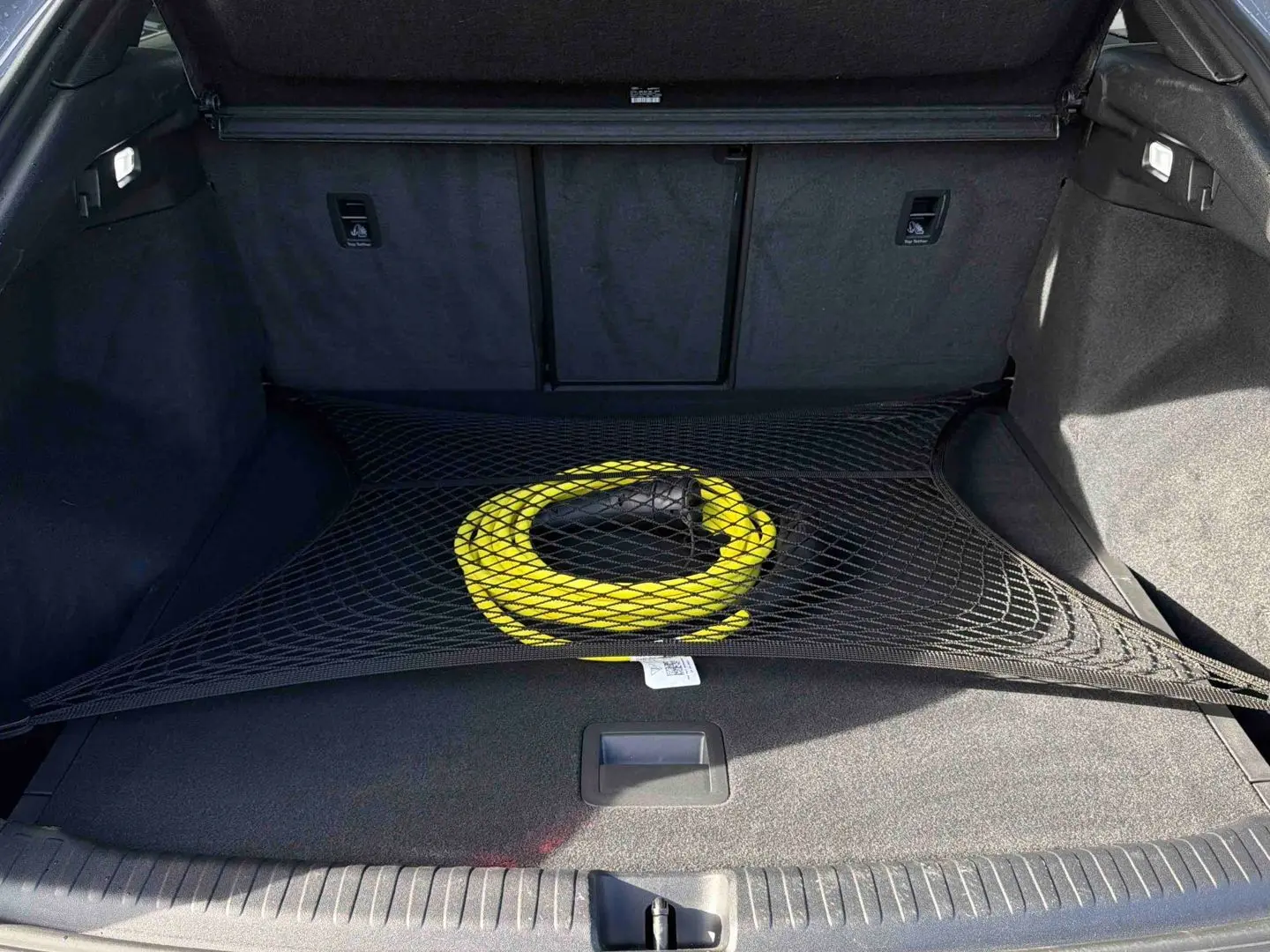 Coffre ouvert de l'Audi Q4 e-tron gris galet avec câble de recharge jaune maintenu par un filet noir.
