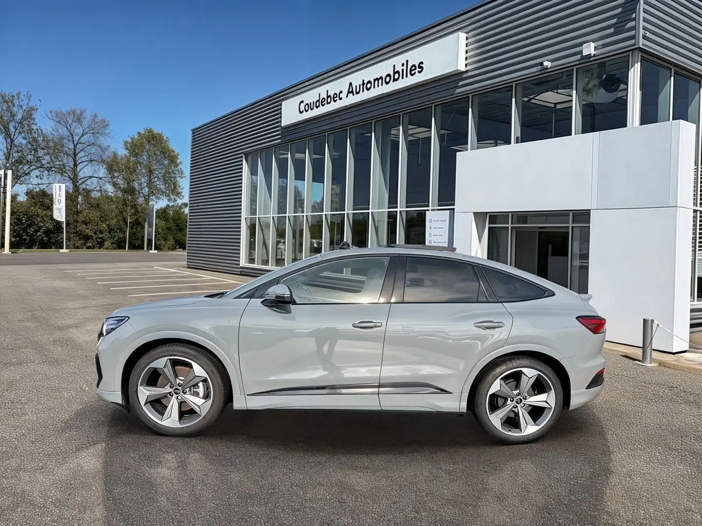 Audi Q4 e-tron gris galet en profil droit, avec jantes 19 pouces à 5 branches, devant un bâtiment moderne.