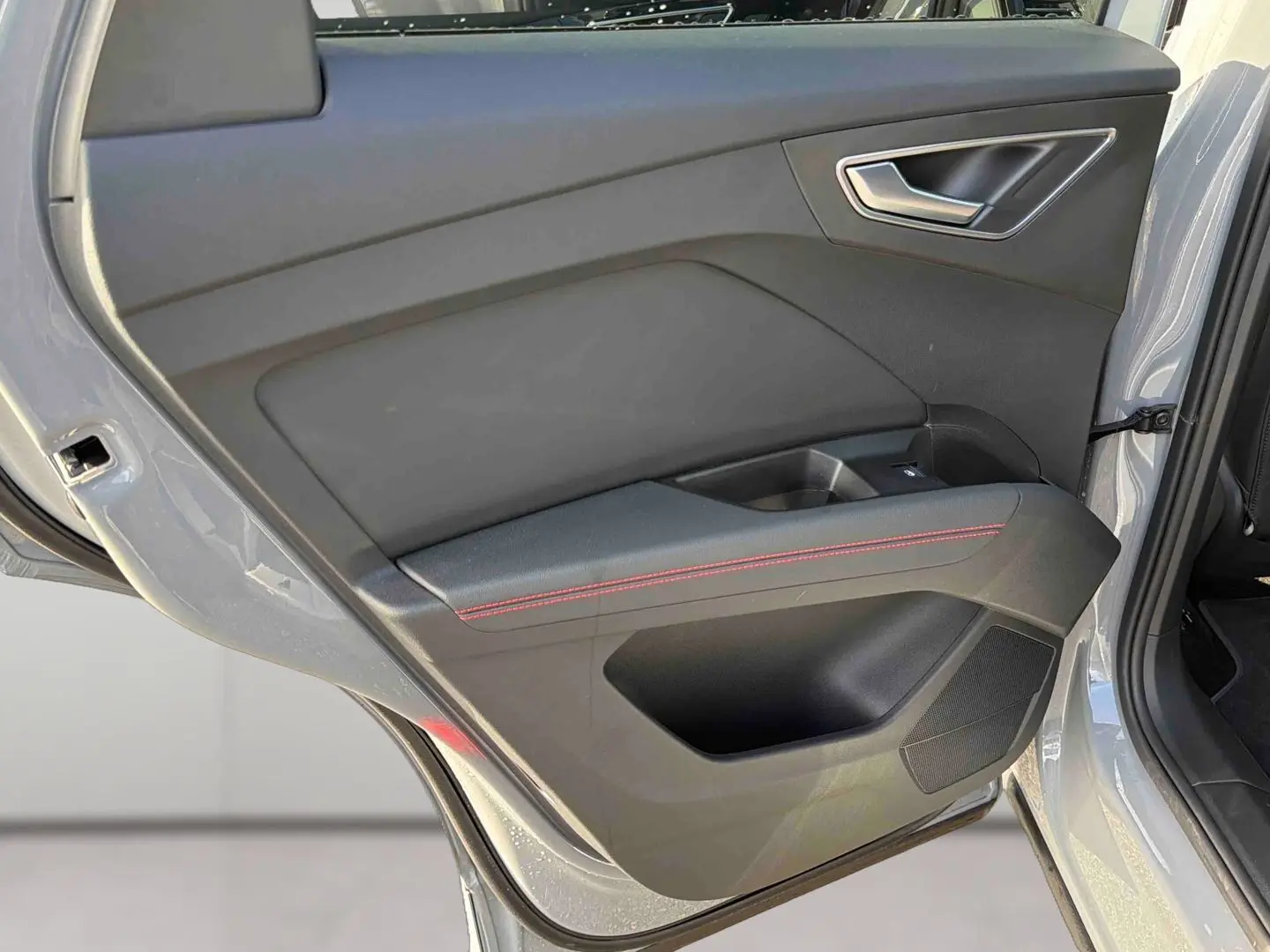 Vue intérieure de la porte arrière gauche gris galet de l'Audi Q4 e-tron avec surpiqûres rouges et poignée argentée.