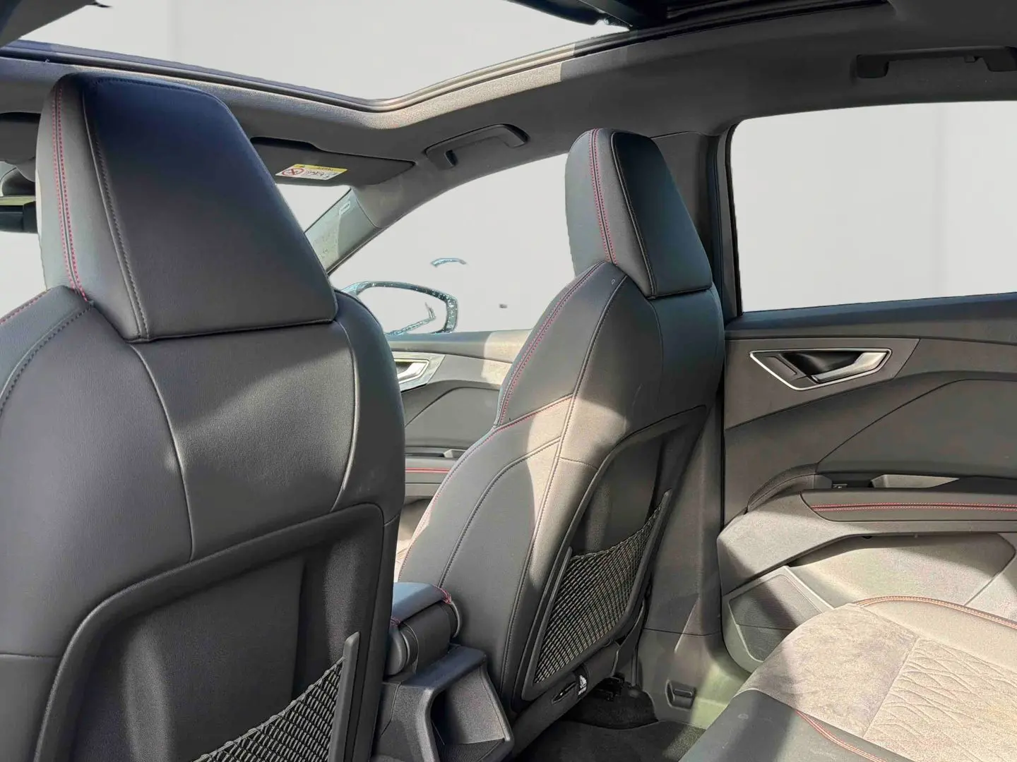 Vue intérieure arrière droite de l'Audi Q4 e-tron 2025 avec sièges en cuir noir et surpiqûres rouges, toit ouvrant panoramique.