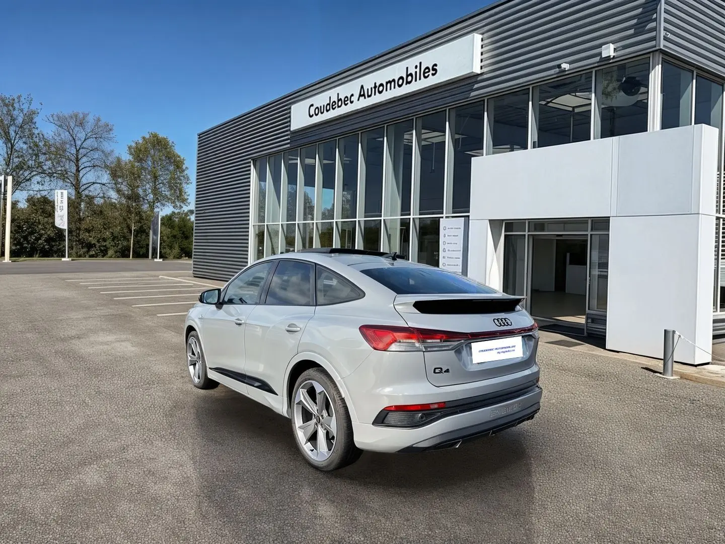 Audi Q4 e-tron gris galet vue 3/4 arrière droit, avec jantes 19 pouces et toit panoramique noir.