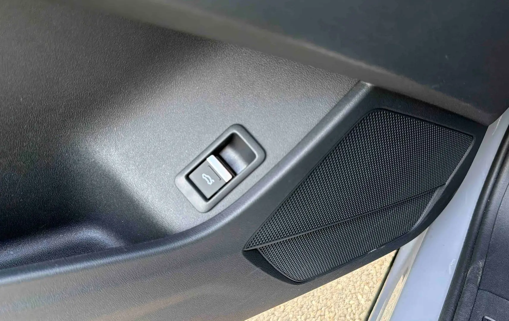 Détail de la porte côté conducteur de l'Audi Q4 e-tron 2025 gris galet avec bouton d'ouverture de coffre et haut-parleur intégré.