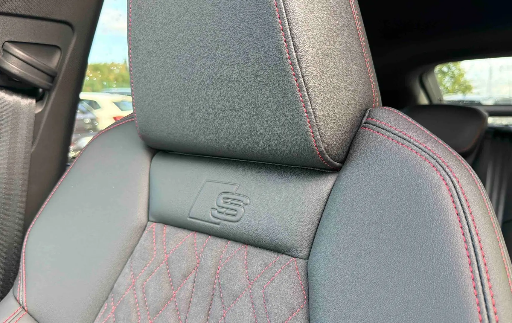 Gros plan sur le siège avant gris foncé avec surpiqûres rouges et logo S embossé, intérieur Audi Q4 e-tron 2025.