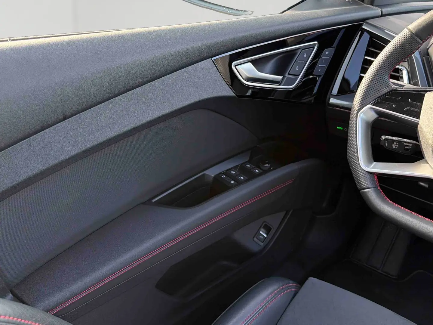Détail intérieur côté gauche de la porte avant avec surpiqûres rouges et commandes de vitres sur Audi Q4 e-tron.