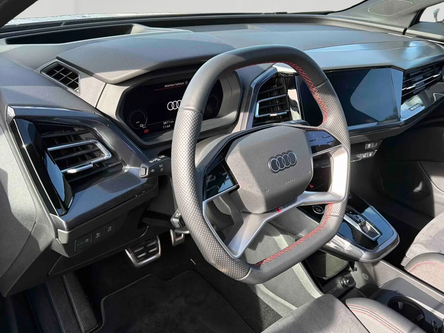 Vue intérieure du volant multifonction noir avec surpiqûres rouges et tableau de bord digital de l'Audi Q4 e-tron 2025.
