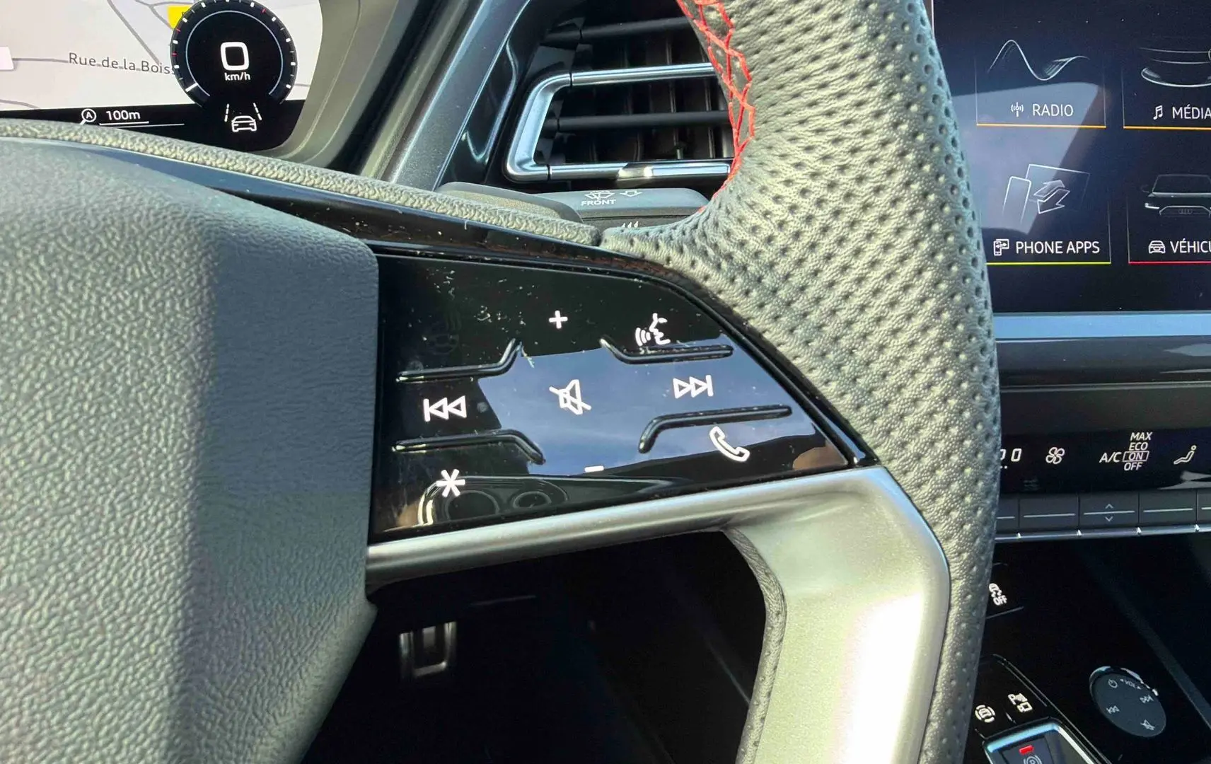 Gros plan sur le volant en cuir perforé avec commandes tactiles à droite, tableau de bord numérique et écran central visibles.