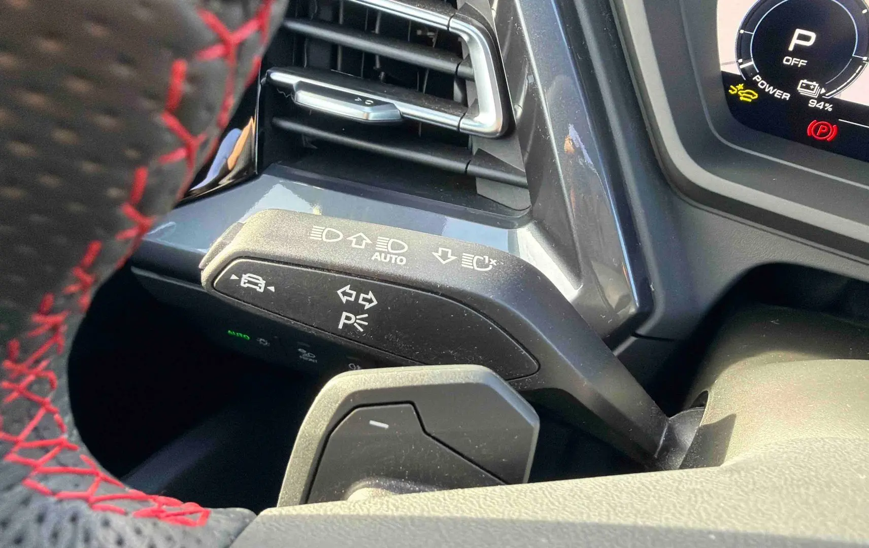 Gros plan sur la commande de clignotants à gauche du volant avec surpiqûres rouges dans un Audi Q4 e-tron gris galet.