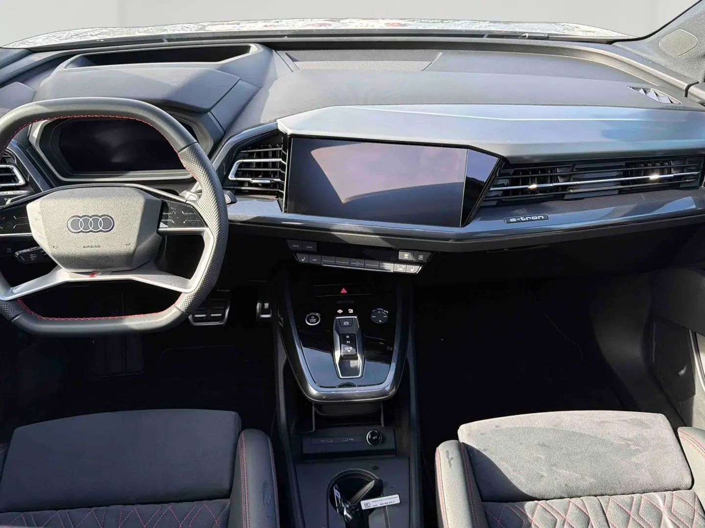 Intérieur Audi Q4 e-tron 2025 vu de face, tableau de bord moderne noir avec écran tactile et volant multifonction cuir.