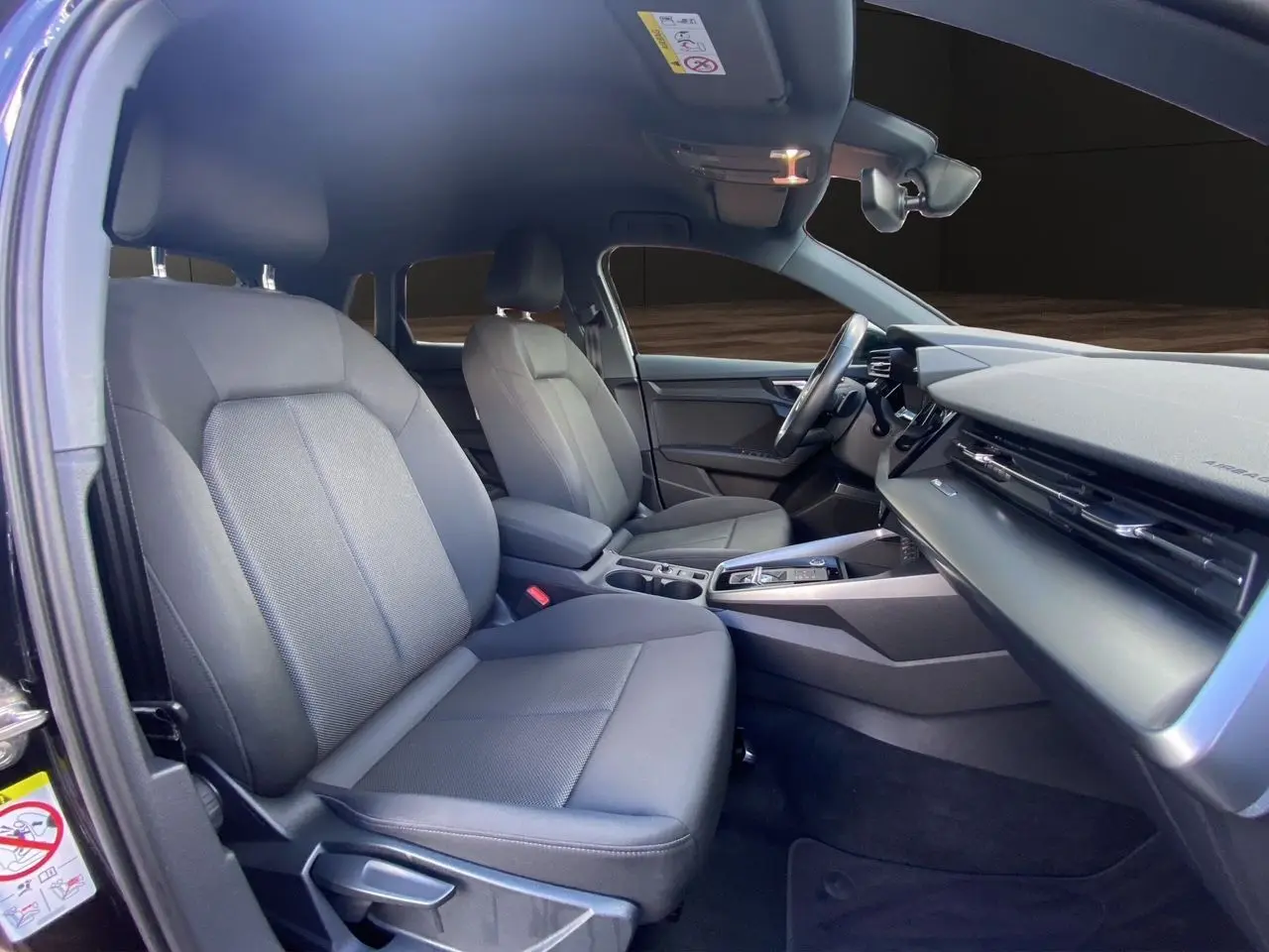 Vue intérieure côté conducteur de l'Audi A3 Sportback 2021 noire, montrant sièges tissu noir et tableau de bord moderne.