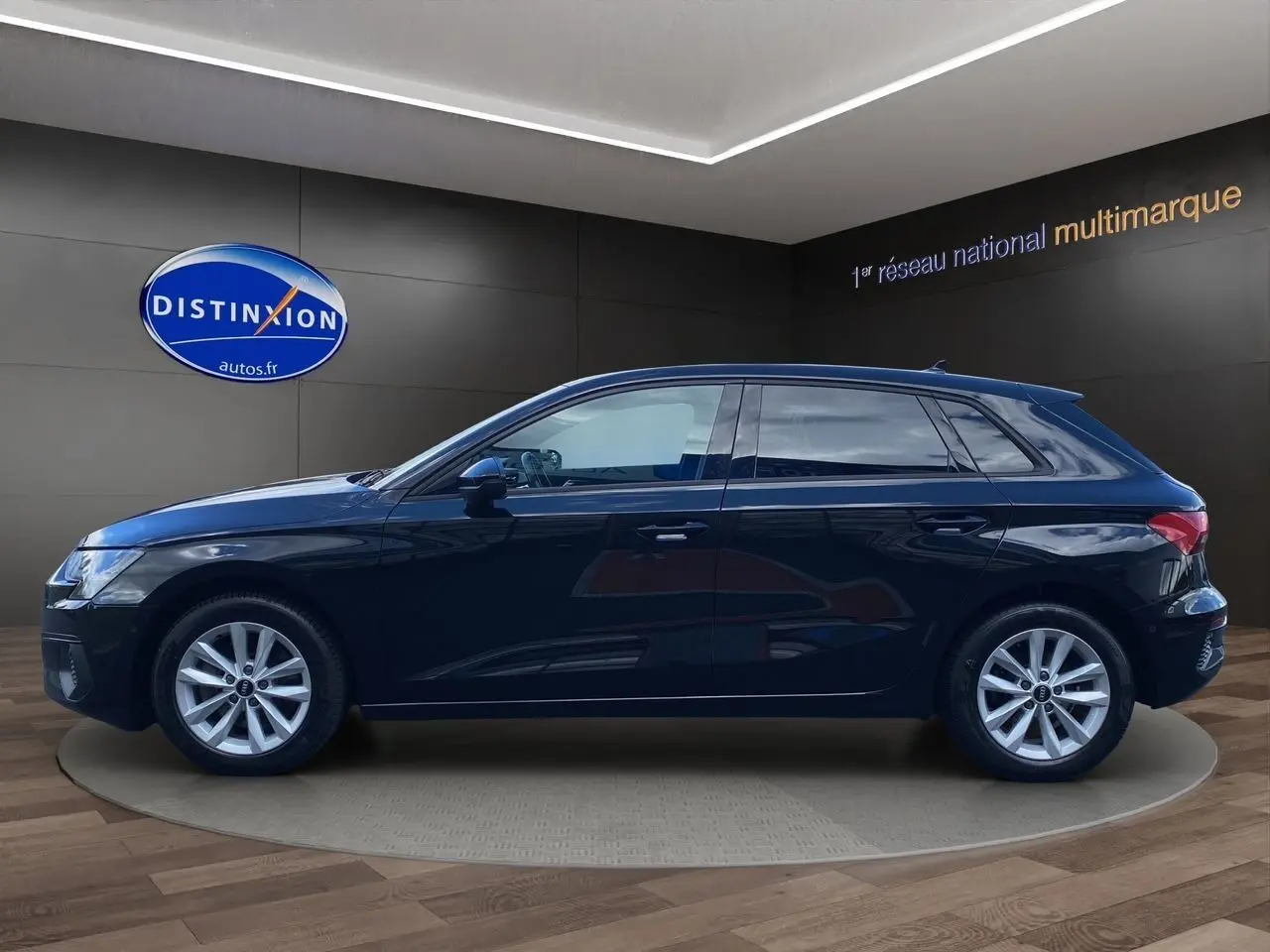 Profil côté gauche d'une Audi A3 Sportback noire 2021, en intérieur sur socle rotatif avec jantes argentées.