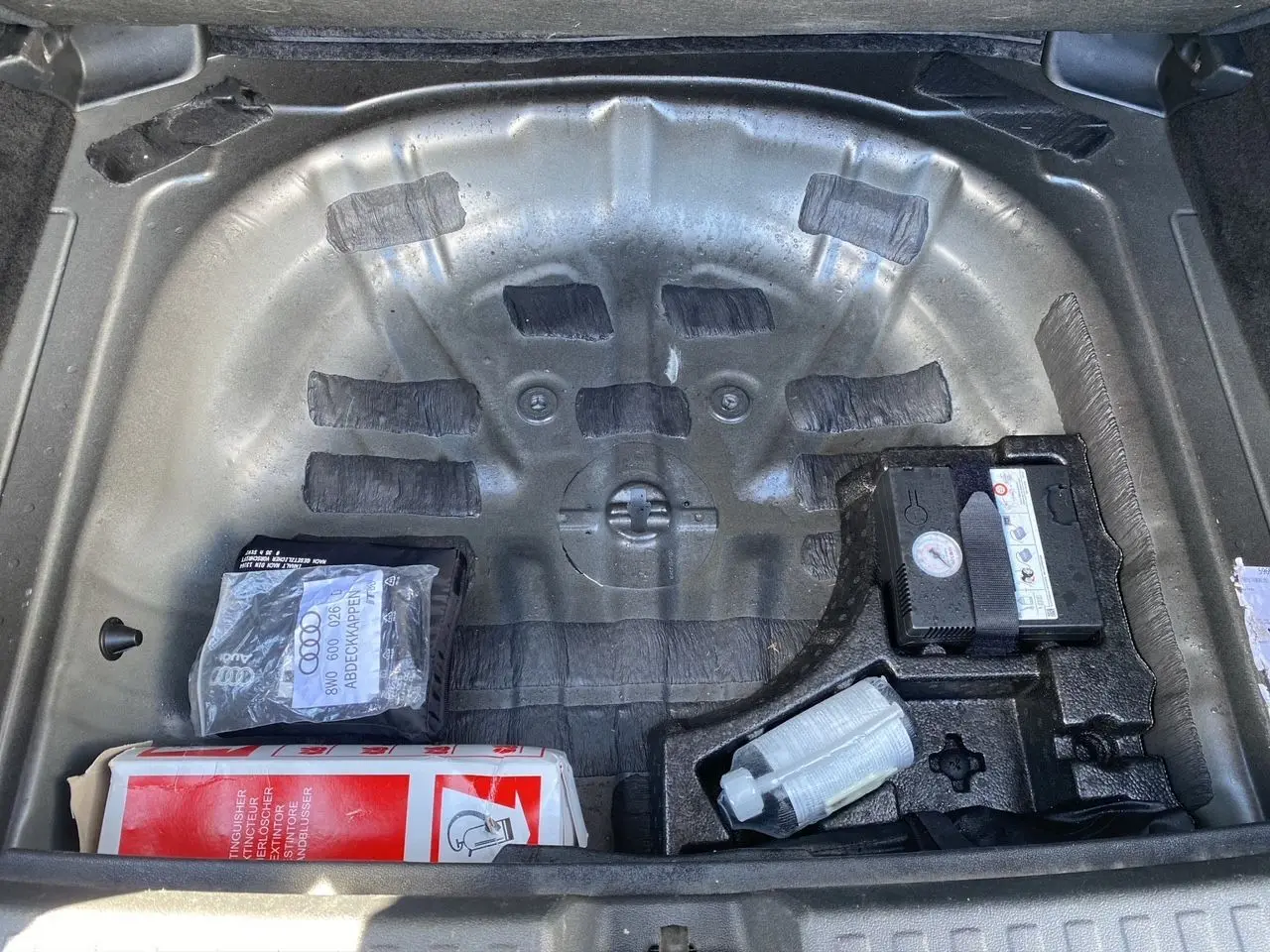 Coffre ouvert d'une Audi A3 Sportback noire, vue plongeante sur le compartiment de roue de secours avec kit de réparation.