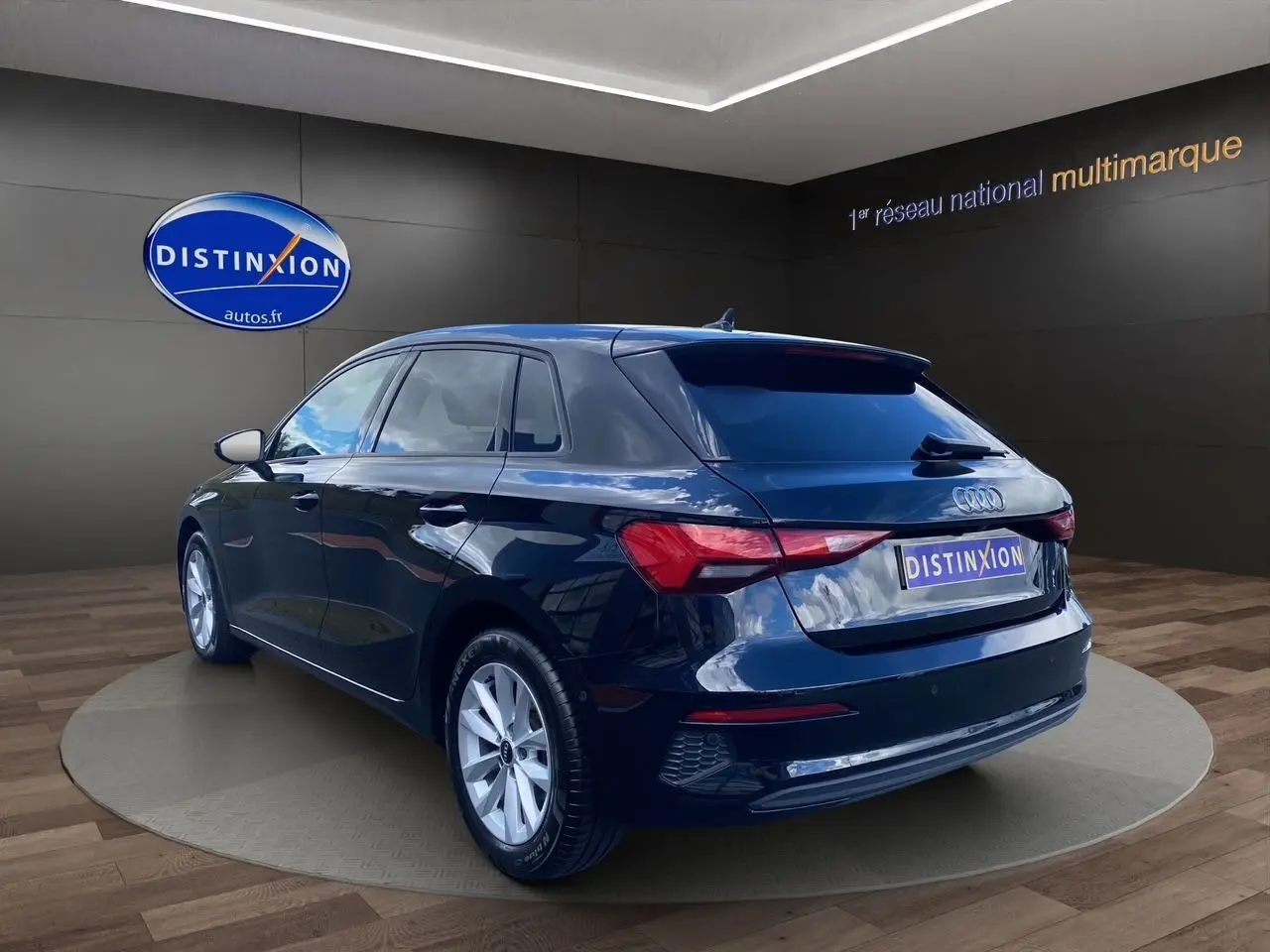 Audi A3 Sportback noir vue 3/4 arrière droit en intérieur avec logo Distinxion sur fond sombre