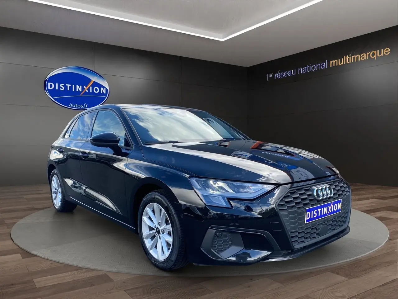 Audi A3 Sportback noire vue 3/4 avant droit, avec calandre hexagonale et jantes argentées en showroom