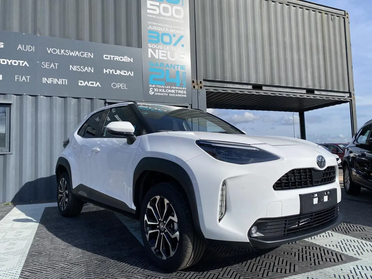 Toyota Yaris Cross blanc pur vue 3/4 avant droit avec jantes alliage et rétroviseurs blancs sur fond urbain.