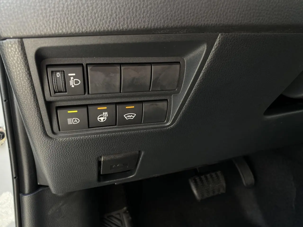 Gros plan sur les commandes sous le tableau de bord côté gauche du Toyota Yaris Cross blanc 2025 hybride.