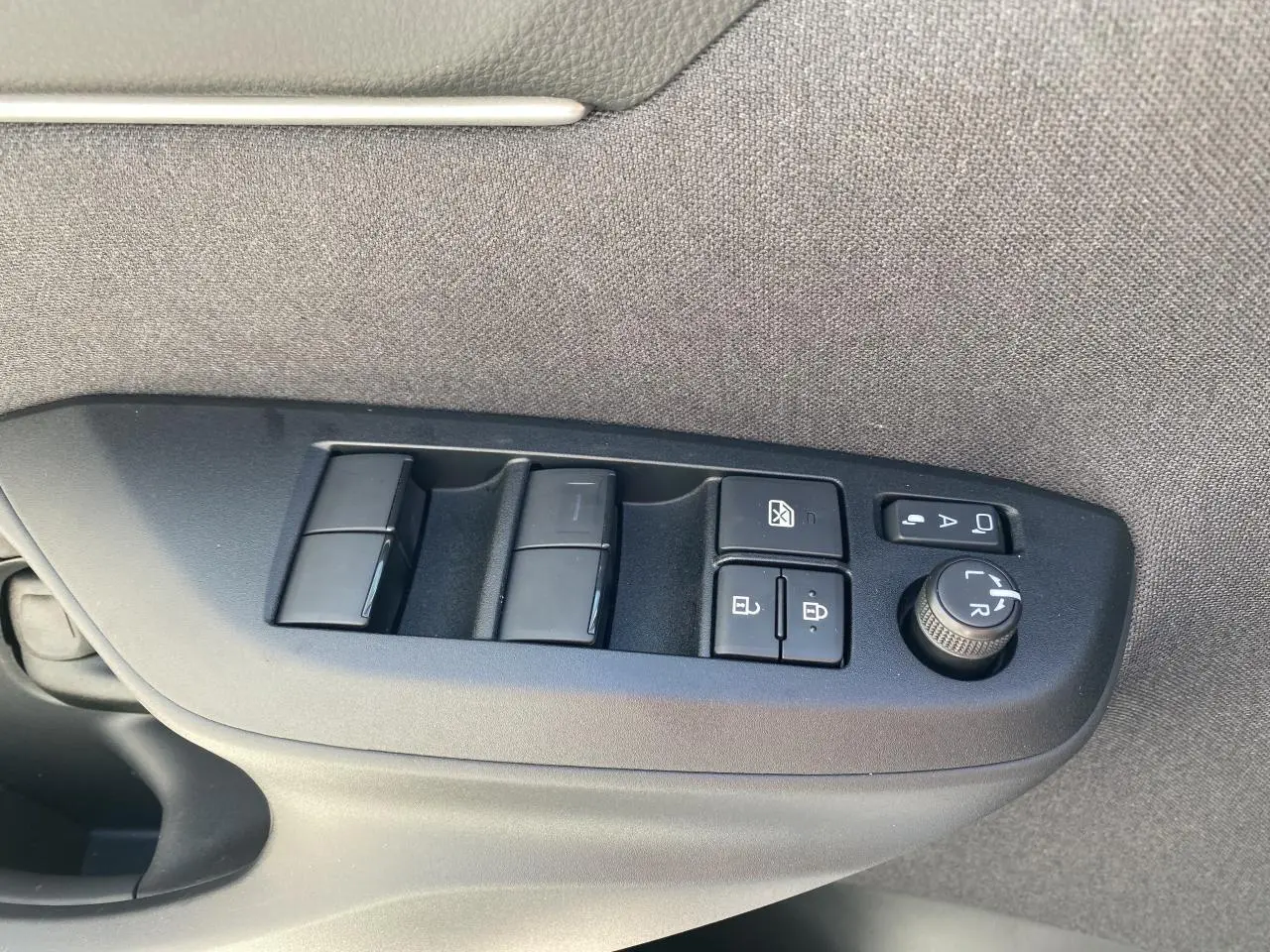 Gros plan sur les commandes de lève-vitres et réglages des rétroviseurs côté conducteur d'une Toyota Yaris Cross blanche.