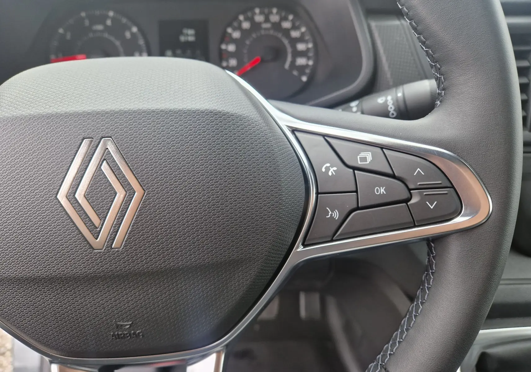 Vue rapprochée du volant cuir du Renault Trafic Fourgon gris urbain 2025, avec commandes multifonctions à droite.
