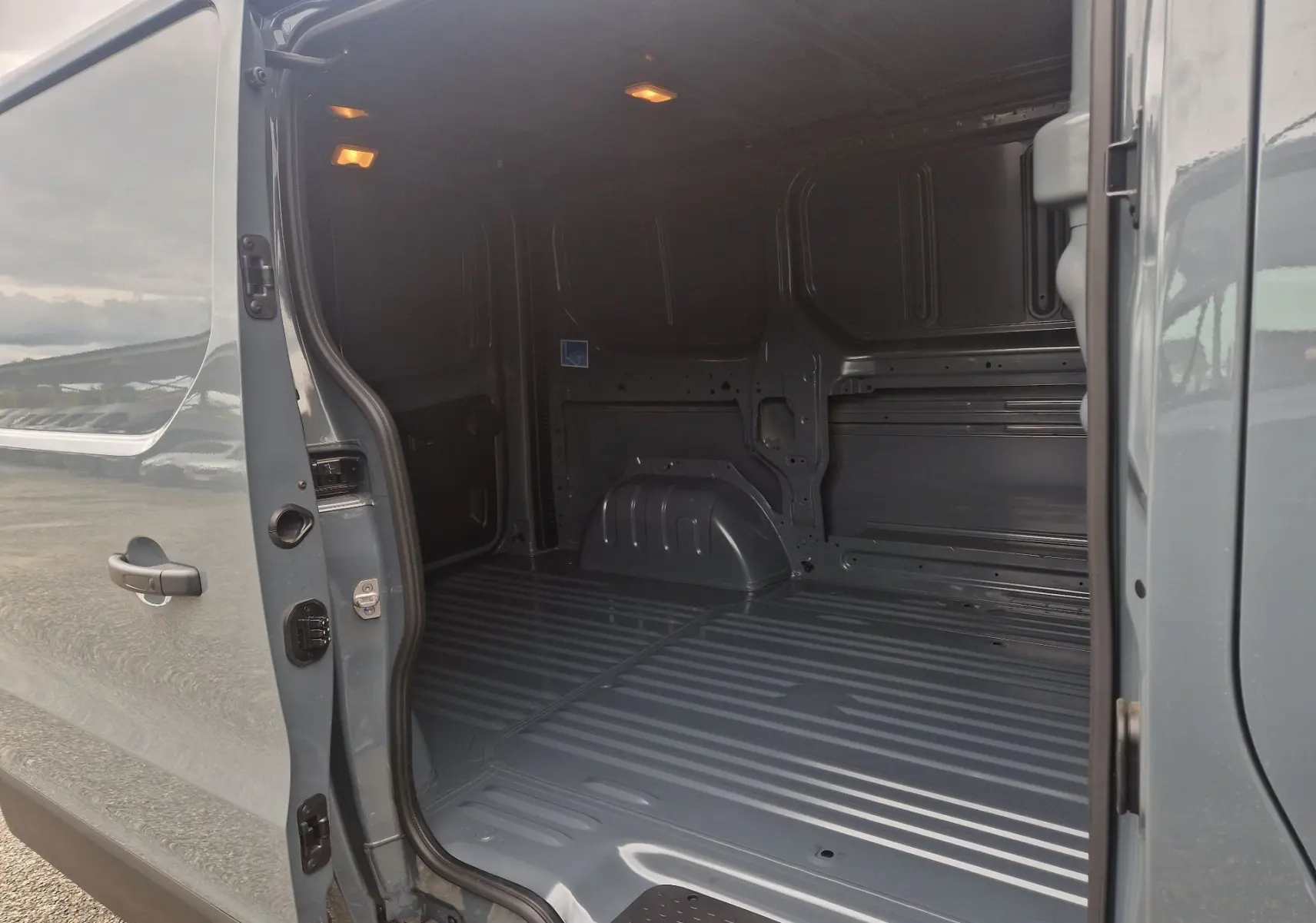 Vue latérale gauche sur l'ouverture du fourgon Renault Trafic L1H1 gris urbain, montrant l'espace de chargement vide et éclairé.