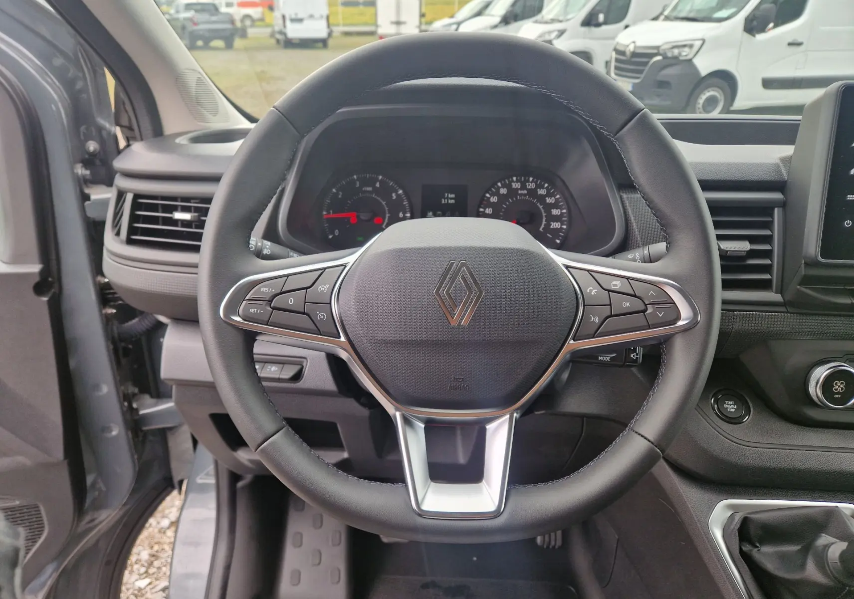 Vue intérieure centrée sur le volant du Renault Trafic Fourgon gris urbain 2025 avec commandes intégrées et tableau de bord visible.