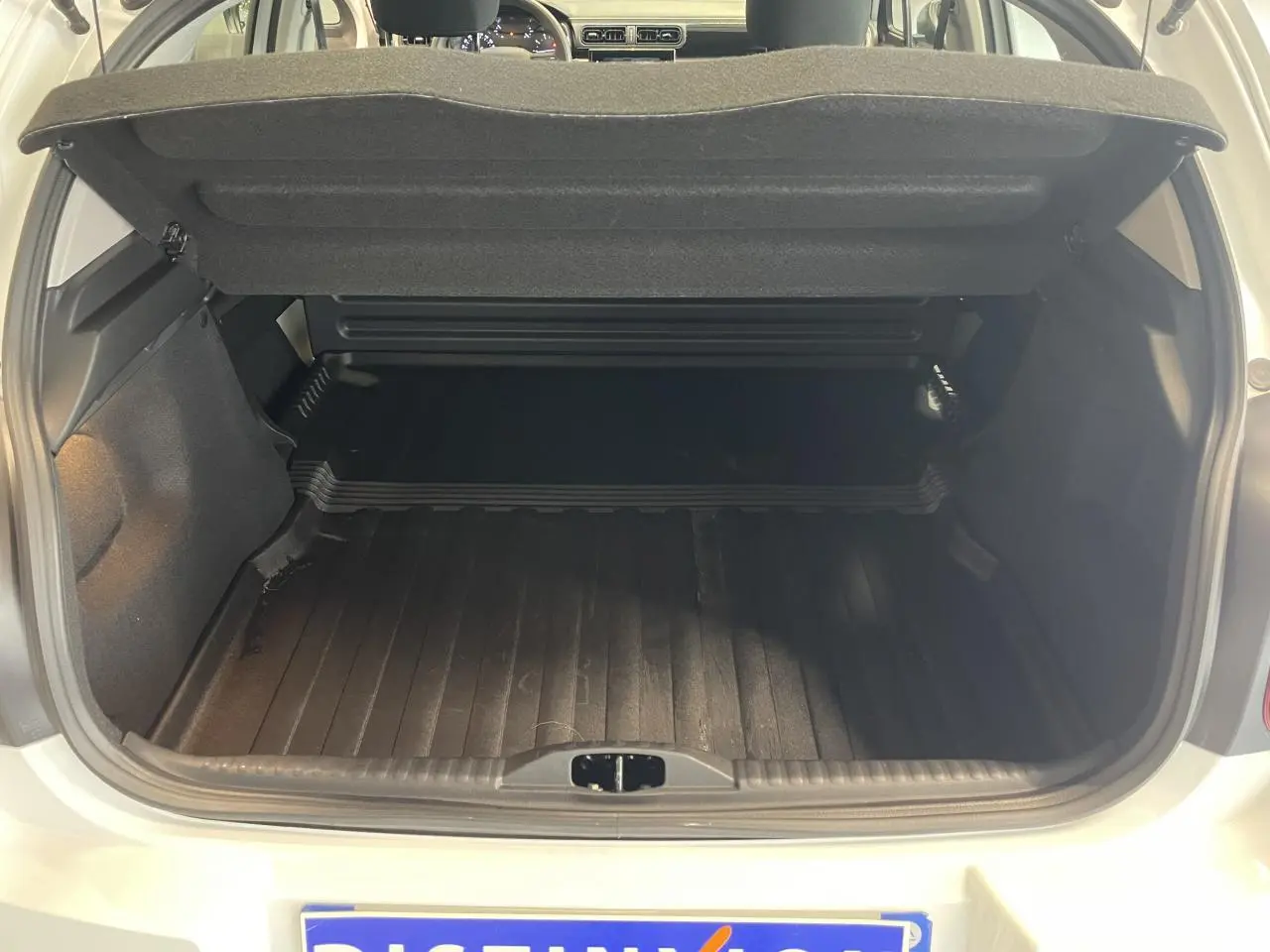 Coffre ouvert vu de l'arrière d'une Citroën C3 blanche 2023, avec tapis de coffre noir et cache-bagages relevé.