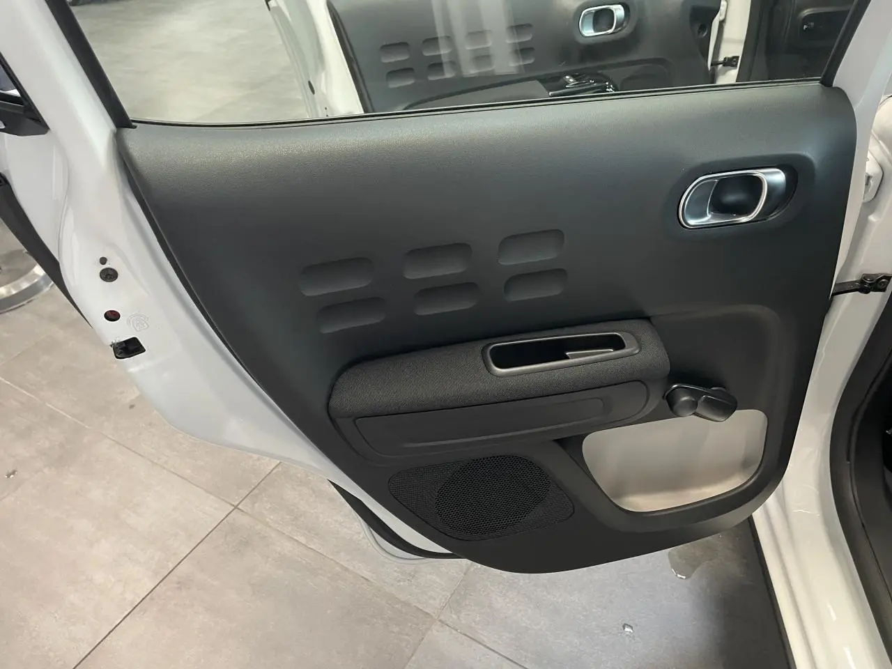 Vue rapprochée de la porte arrière gauche noire avec manivelle sur une Citroën C3 blanche 2023.