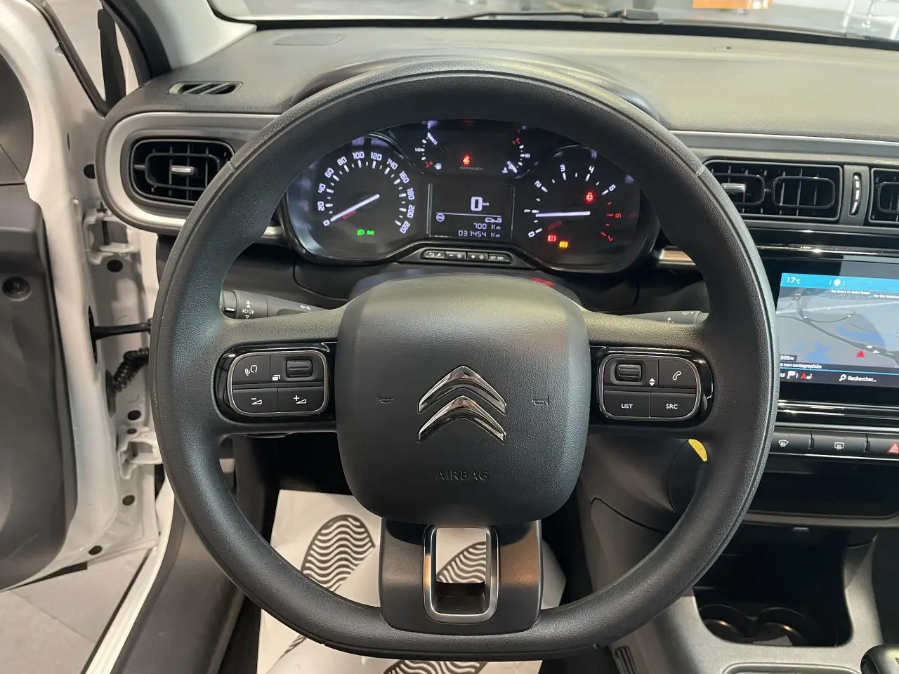 Vue intérieure centrée sur le volant noir de la Citroën C3 blanche, avec tableau de bord et écran tactile visibles.