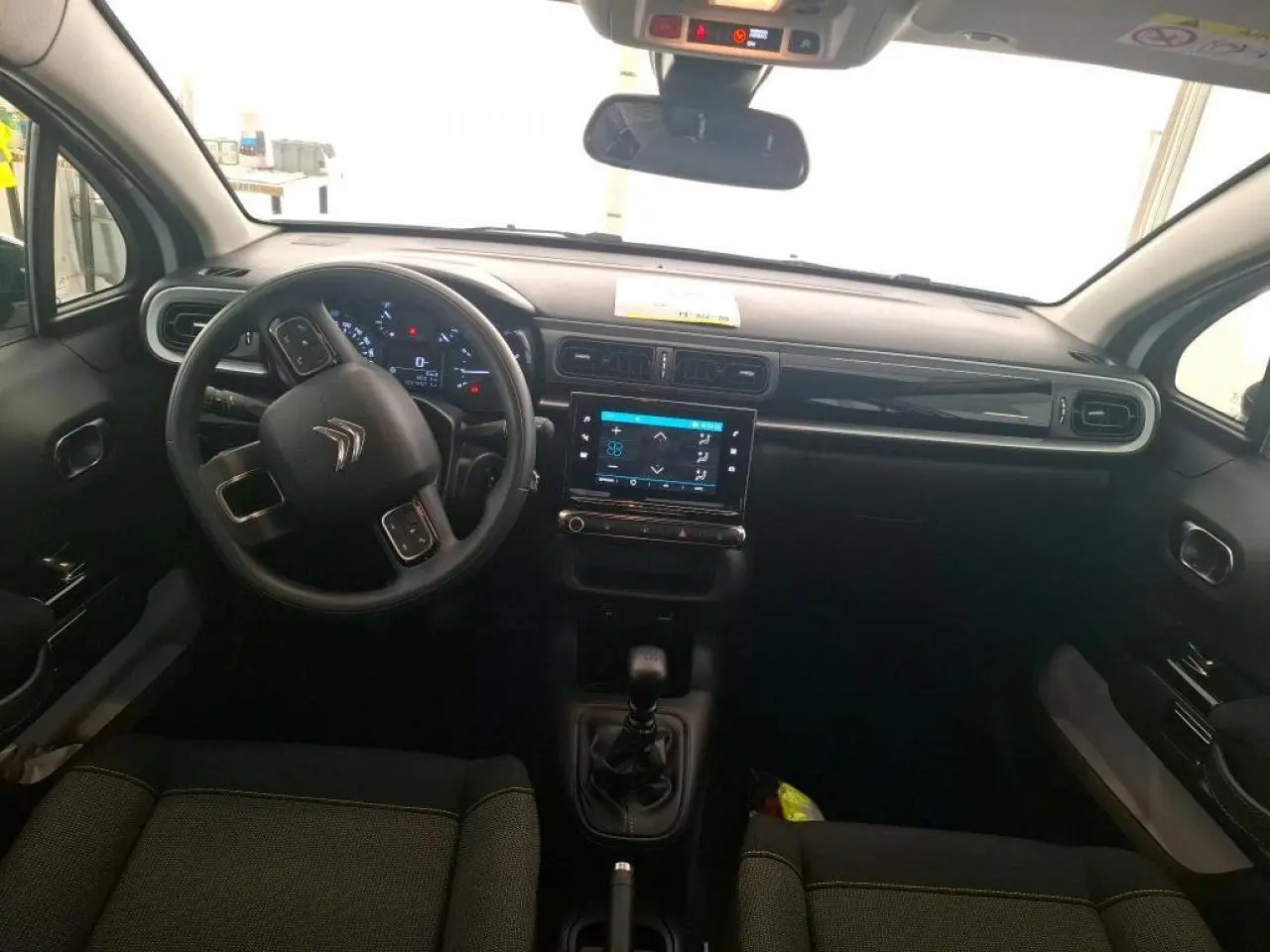 Vue intérieure avant du tableau de bord et volant noir de la Citroën C3 blanche avec écran tactile central allumé.