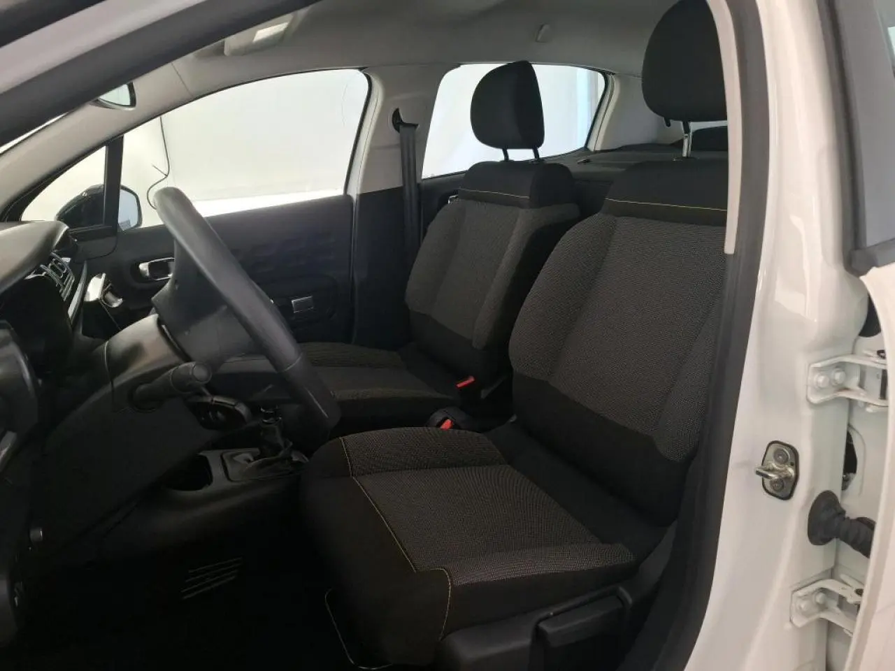 Vue intérieure côté conducteur d'une Citroën C3 blanche 2023 avec sièges tissu gris et volant réglable.
