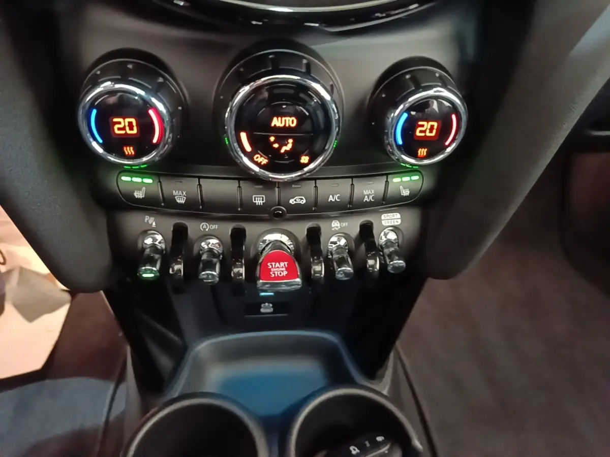 Vue rapprochée du tableau de bord central de la MINI Cooper Edition Premium Plus 2023 avec commandes climatisation et bouton start/stop rouge.