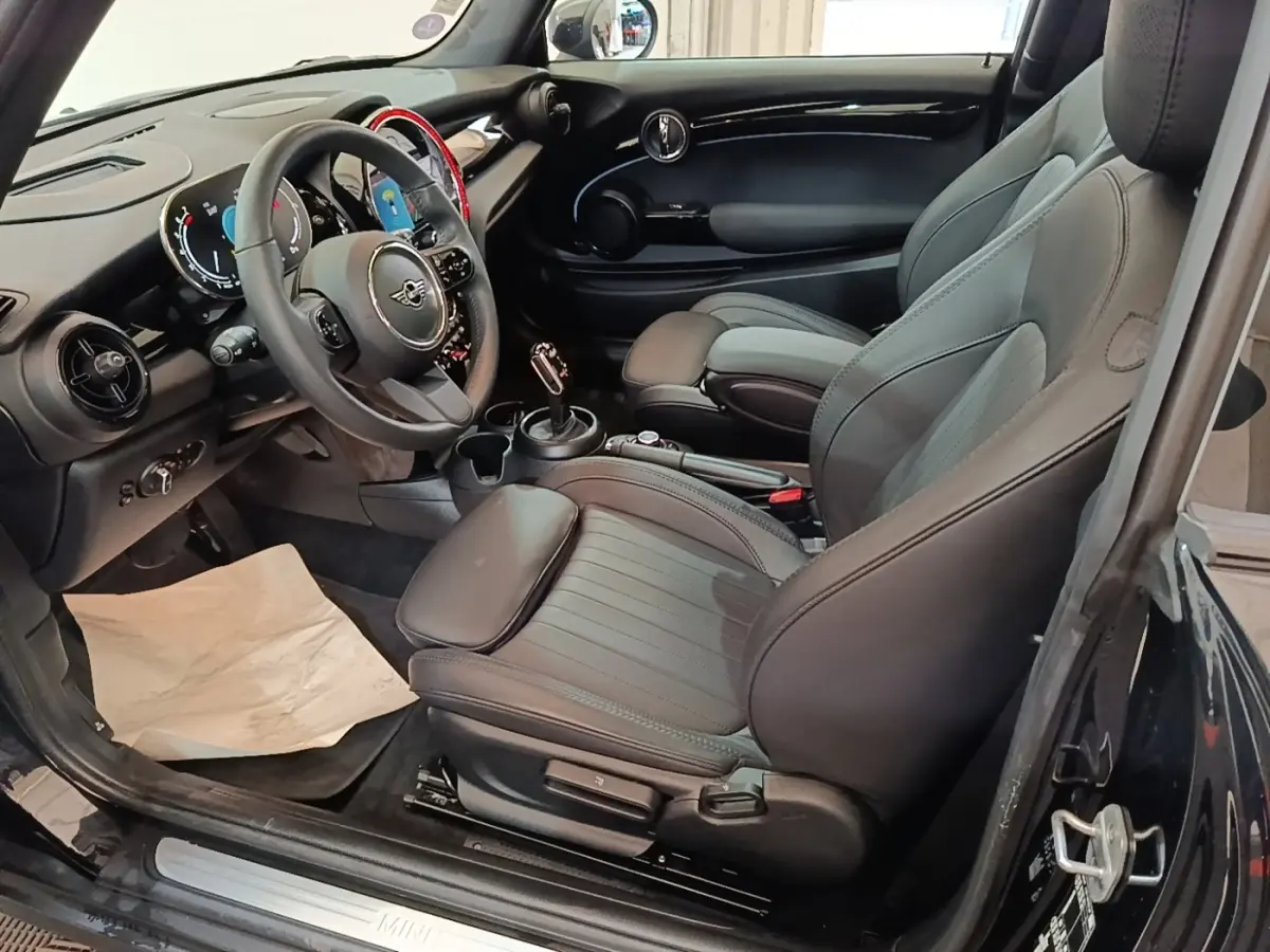Intérieur noir de la MINI Cooper Premium Plus 2023 vu côté conducteur, avec sièges sport et volant cuir multifonctions.