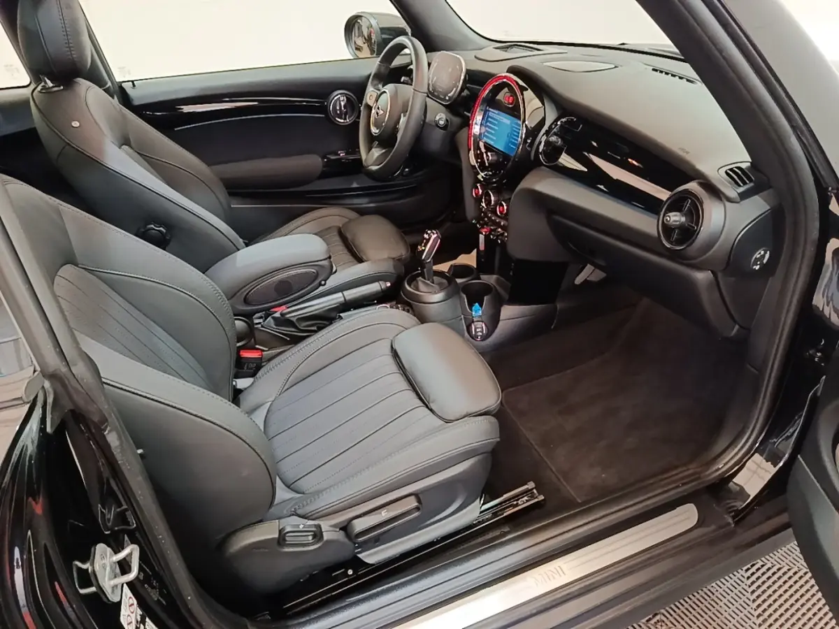 Intérieur noir de la MINI Cooper Premium Plus 2023 vu côté conducteur, avec tableau de bord digital et sièges sport cuir.