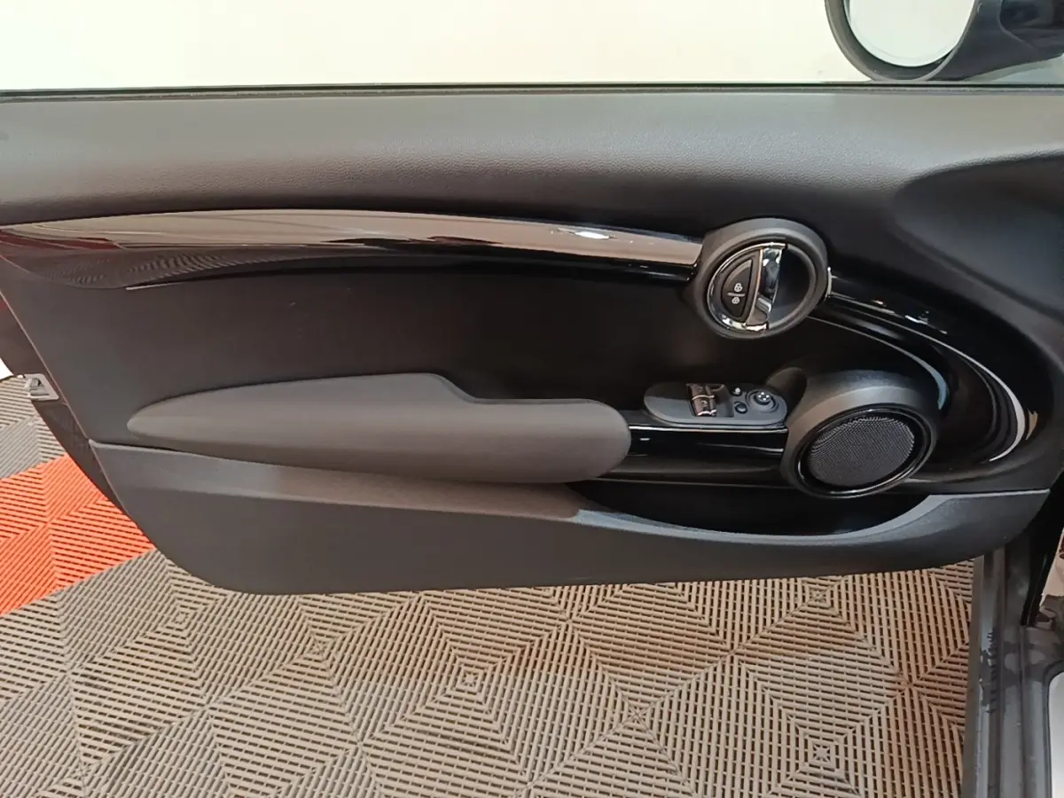 Gros plan sur la porte intérieure côté conducteur de la MINI Cooper noire, avec commandes de vitres et haut-parleur rond.