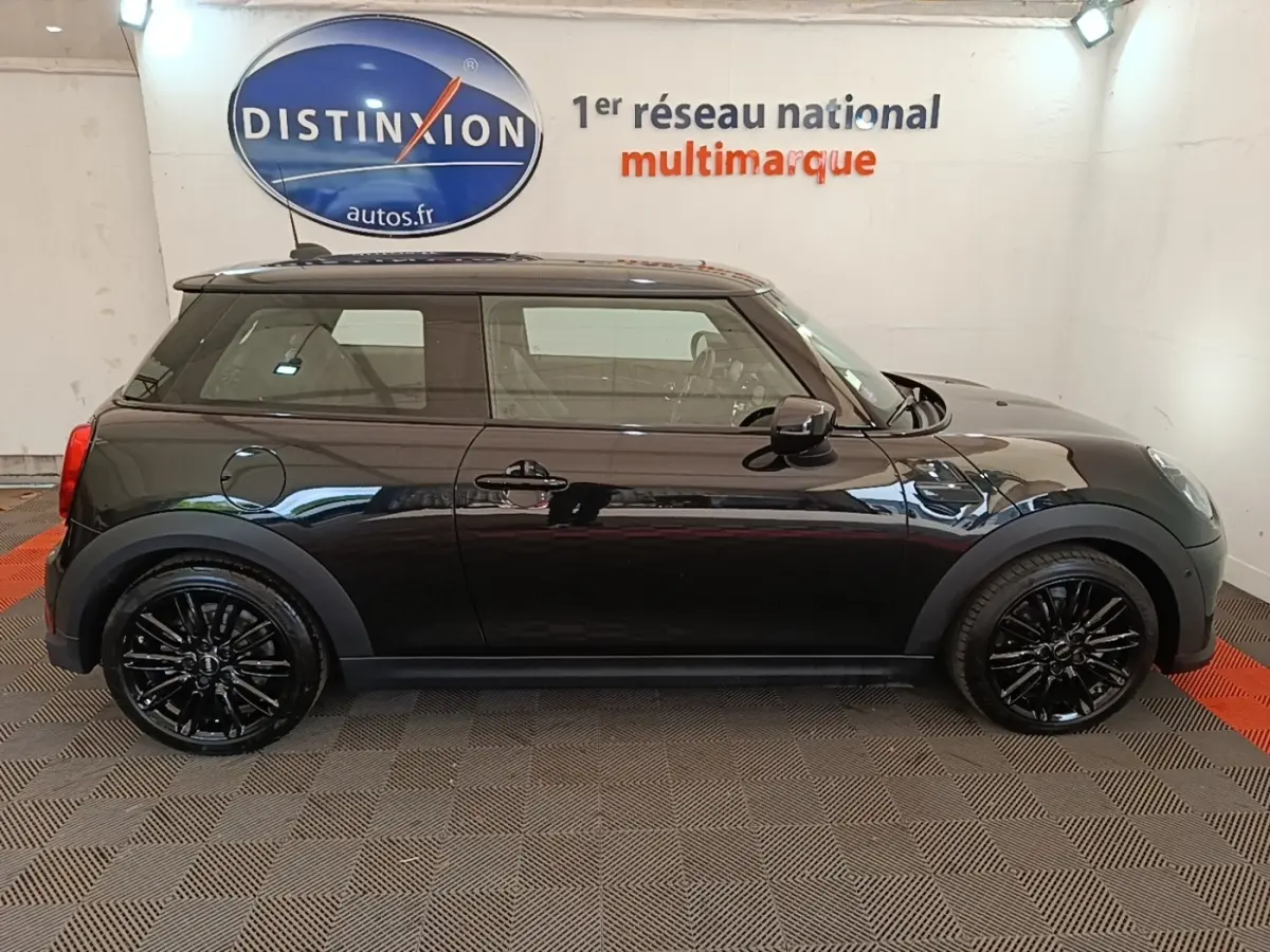 Profil côté gauche d'une MINI Cooper Edition Premium Plus noire 3 portes avec jantes noires brillantes en intérieur showroom.