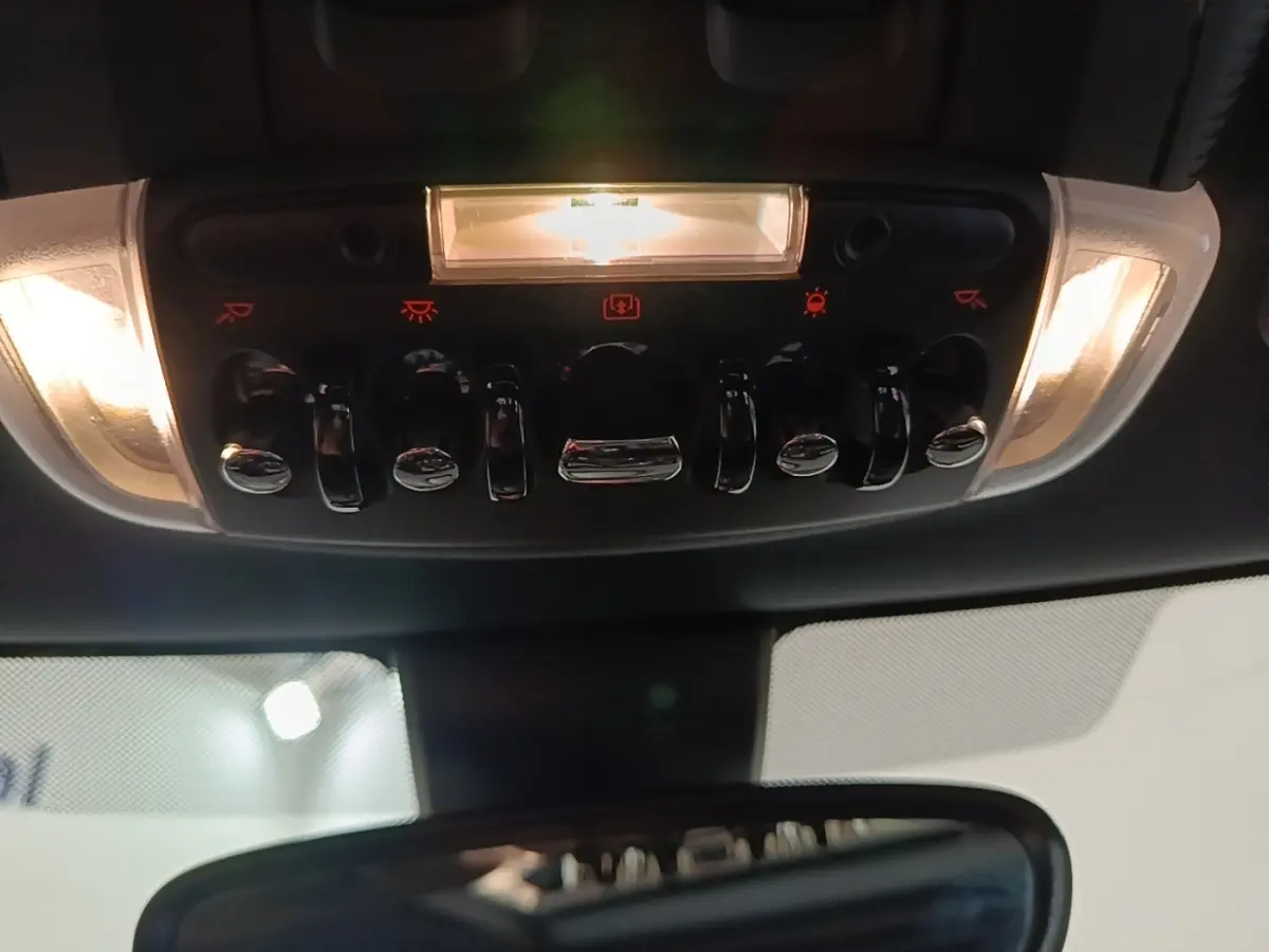 Vue intérieure du panneau de commandes de plafonnier avec interrupteurs chromés et éclairage, MINI Cooper 2023 noir.