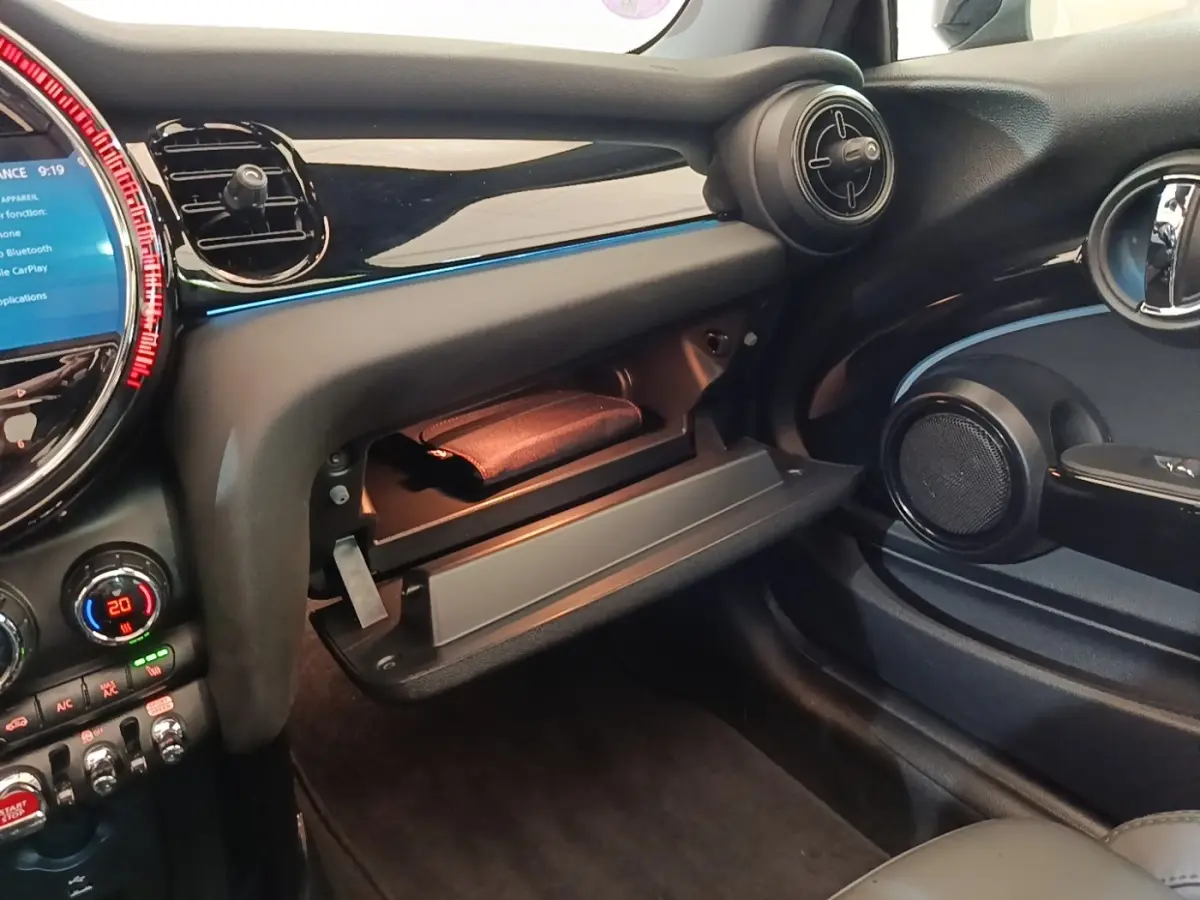 Vue intérieure côté passager de la MINI Cooper Edition Premium Plus 2023 noire, avec boîte à gants ouverte et tableau de bord noir brillant.