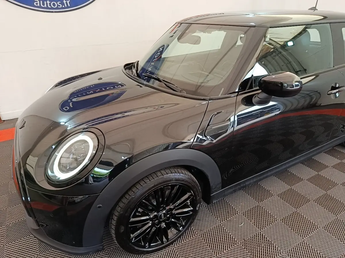 Vue 3/4 avant droit d'une MINI Cooper Edition Premium Plus noire avec jantes noires et phares LED circulaires allumés.
