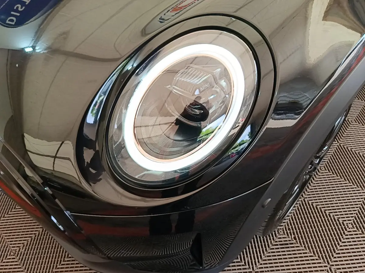 Gros plan sur le phare avant gauche LED d’une MINI Cooper Edition Premium Plus noire, soulignant son design circulaire moderne.