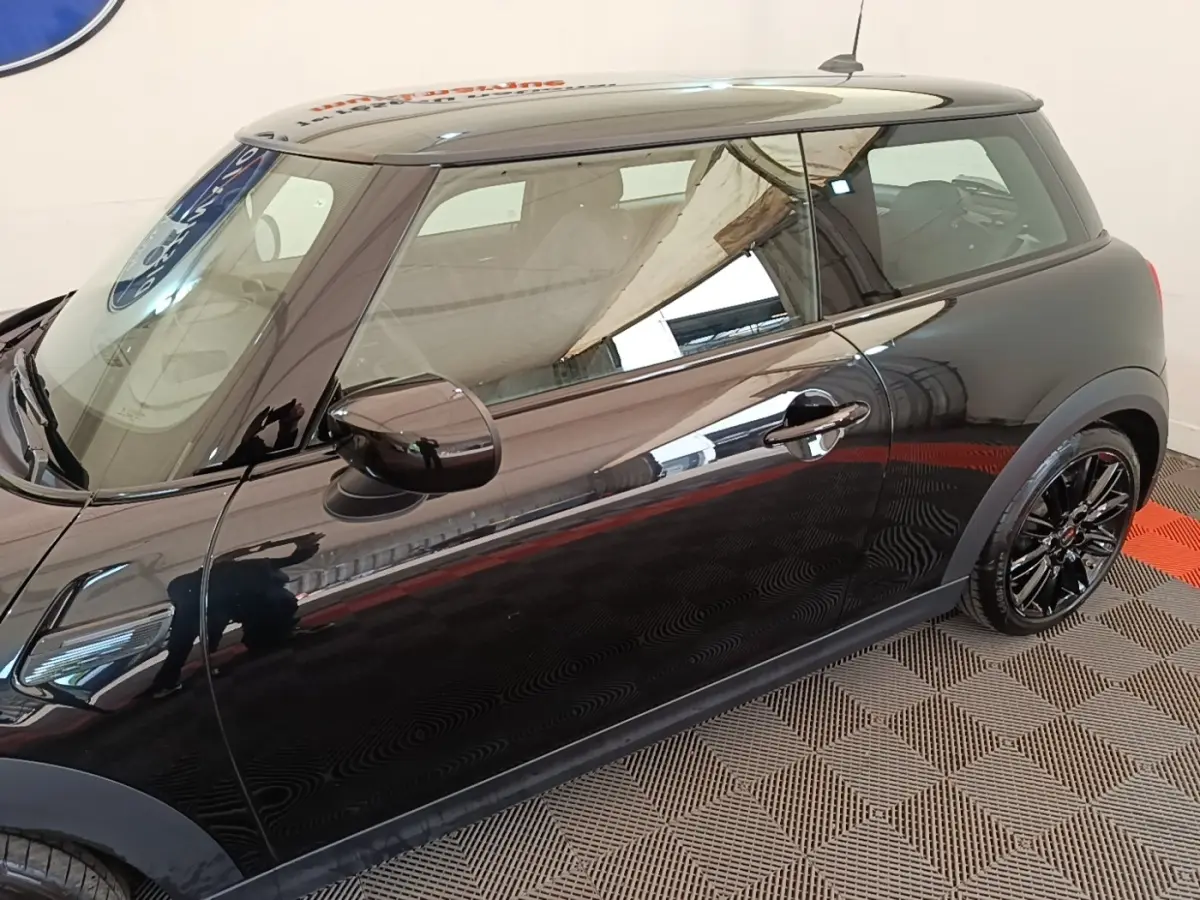 Vue de profil côté gauche d'une MINI Cooper noire avec jantes noires brillantes sur sol à damier.