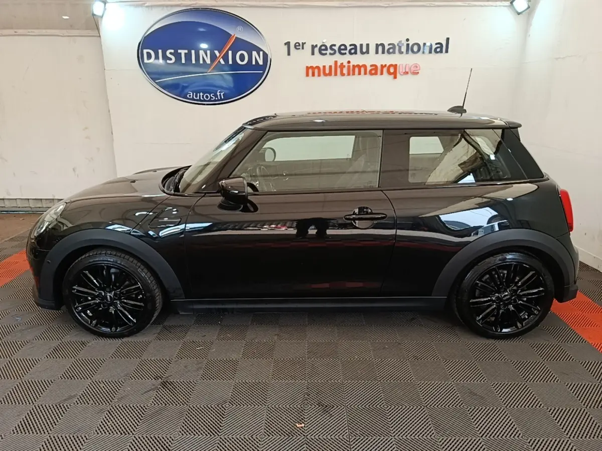 Profil droit d'une MINI Cooper Edition Premium Plus noire 3 portes avec jantes noires brillantes en intérieur showroom.