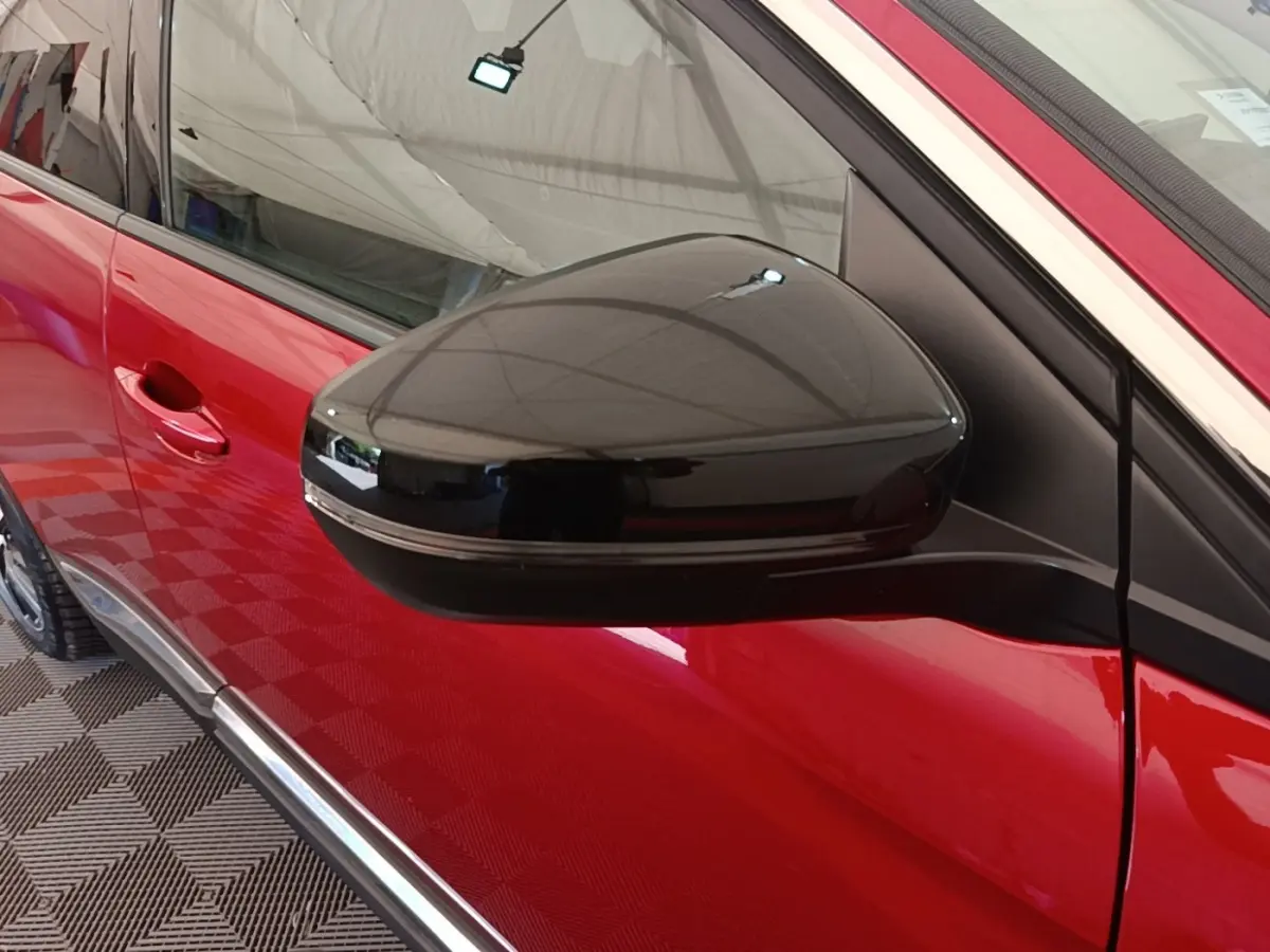 Gros plan sur le rétroviseur noir côté conducteur d’un Peugeot 3008 rouge, avec poignée de porte visible.