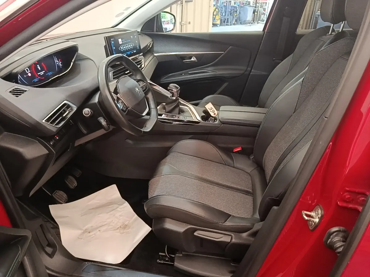 Vue intérieure côté conducteur d'un Peugeot 3008 rouge, avec tableau de bord numérique et sièges tissu-cuir noirs.