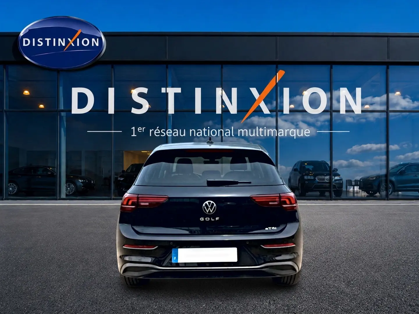 Vue arrière d'une Volkswagen Golf noire 2026 avec feux arrière LED, garée devant une vitrine Distinxion.