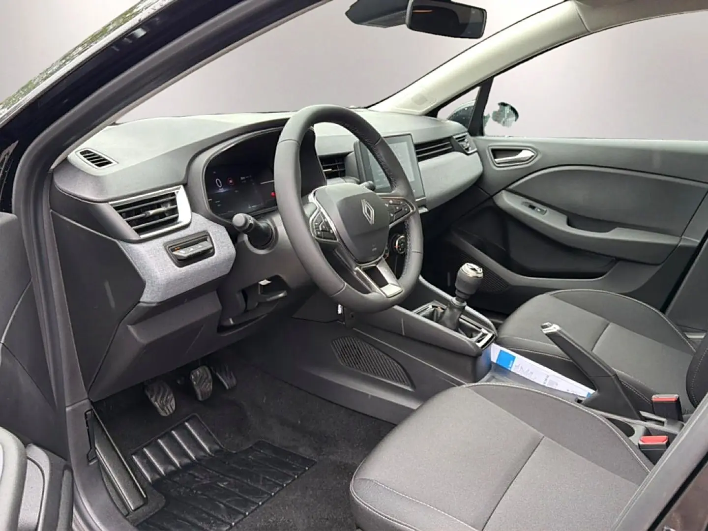 Vue intérieure côté conducteur de la Renault Clio V noire, montrant le volant multifonction et la boîte manuelle.