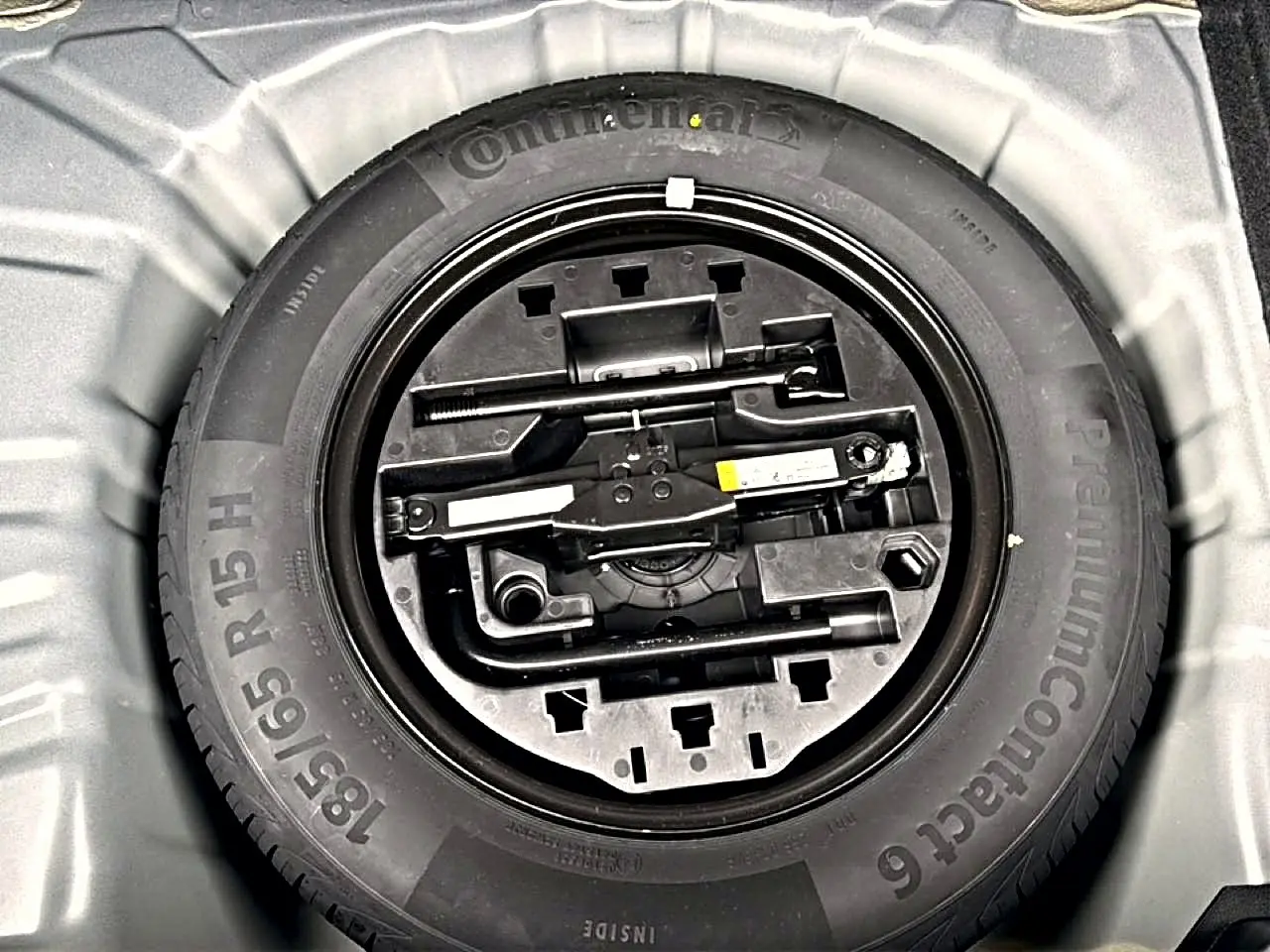 Roue de secours avec kit d'outils intégrés dans le coffre d'une Renault Clio V noire, vue de dessus.